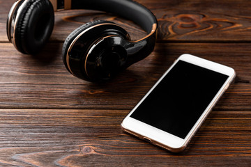 Mobile phone and wireless headphones on wooden background.