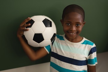 Front view of black schoolboy holding football and looking at