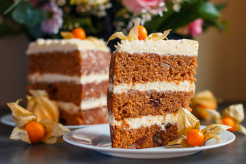 Two slices of homemade carrot cake with nuts, pears and cream-cheese and physalis as decoration on the plates with a basket of fresh flowers on the background
