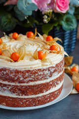 Homemade carrot cake with nuts, pears and cream-cheese and physalis as decoration on the plate with a basket of fresh flowers on the background