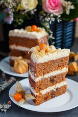 Slice of homemade carrot cake with nuts, pears and cream-cheese and physalis as decoration on the plate with a basket of fresh flowers on the background