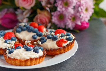 Homemade shortbread cake with whipped cream and fresh berries on the plate, bouquet of flowers on the background