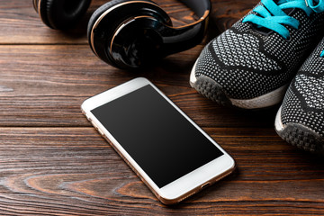 Fitness sneakers and mobile phone with headphones on wooden background. - Powered by Adobe