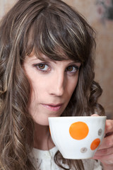 Close up portrait of young woman drinking tea from mug, looking at camera