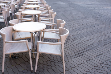 A number of empty tables with chairs are connected by a cable from theft in a cafe on the street.