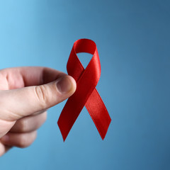 Red ribbon as symbol of aids awareness in hand on blue background