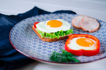 Sandwich with egg, ham, cheese, toast and salad leaves lies on a plate with tomato and dill