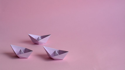three purple paper boats on a light pink background. team work of three colleagues