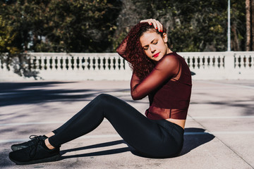 Obraz na płótnie Canvas .Young beautiful latin woman with red curly hair doing exercise outdoors on a sunny winter day. Molding her body to be in good shape. Wearing sport wear. Lifestyle.