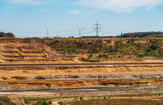 Blick zum Rand einer Braunkohlegrube mit F&ouml;rderb&auml;ndern, Windr&auml;der im Hintergrund