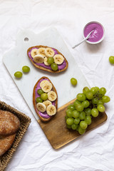 bread dessert sandwiches with yogurt and banana on a rustic cutting board with grapes on white background, top view. Flat lay. Delicious breakfast or snack