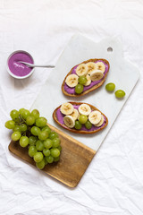 bread dessert sandwiches with yogurt and banana on a rustic cutting board with grapes on white background, top view. Flat lay. Delicious breakfast or snack