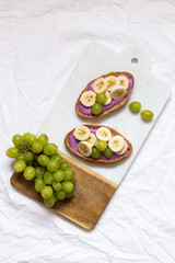 bread dessert sandwiches with yogurt and banana on a rustic cutting board with grapes on white background, top view. Flat lay. Delicious breakfast or snack