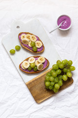 bread dessert sandwiches with yogurt and banana on a rustic cutting board with grapes on white background, top view. Flat lay. Delicious breakfast or snack