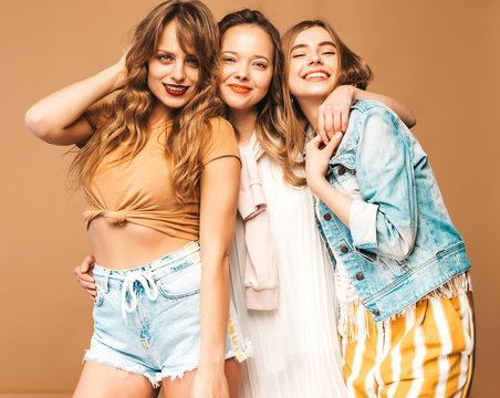 Three young beautiful smiling hipster girls in trendy summer casual clothes. Sexy carefree women posing on golden background. Positive models going crazy