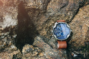 Fashionable elegant men's watch lying outdoors on the stone. Stylish accessories in the nature forest. Copy space place.