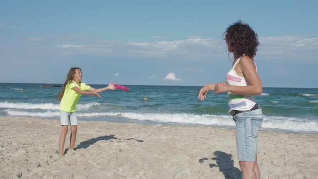 Family at beach playing with flying disc. Little girl with mom play frisbee.