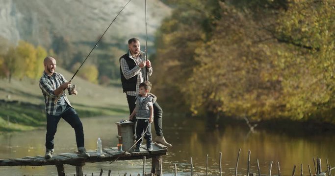 Fishing time for two friends and one small boy on sunny day catching fish with fishing rod. 4k