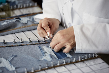 Female worker in white coat pinning distressed jeans to board