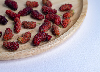 Mulberry fruit mulberry many both purple red orange in the plate made of wood all laid are on a white background.