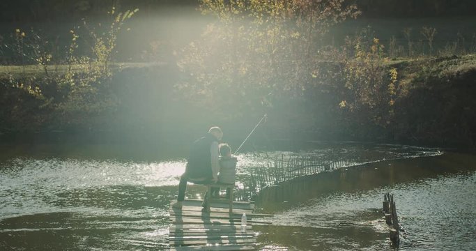 Wonderful view of a lake , dad and His son sitting on a chair in the top of bridge and catching fish from lake. slow motions. 4h