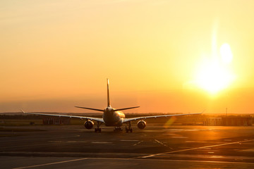 A picture of the plane standing on the side runway and preparing to departure. The sun is going down during the nice evening.