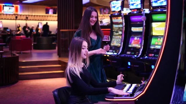 Two girls play casino and drink wine. Beautiful girls in Casino hall.