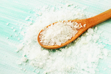 White grains of Sea salt in wooden spoon light blue table background, closeup