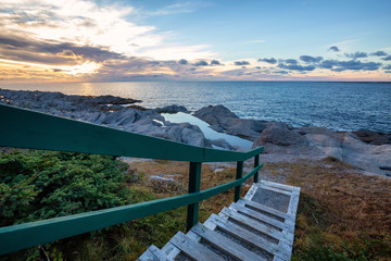Wooden stairs going down to a beautiful rocky Atlantic Ocean Coast during a vibrant sunset. Taken at Cow Head, Newfoundland, Canada.