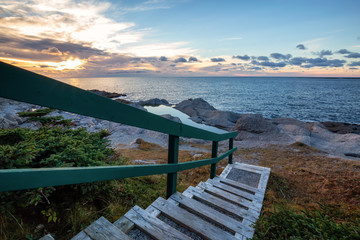 Wooden stairs going down to a beautiful rocky Atlantic Ocean Coast during a vibrant sunset. Taken at Cow Head, Newfoundland, Canada.