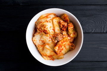 Kimchi in the white plate on the black wooden  background.Top view.Copy space.