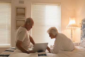 Senior couple using laptop in bedroom