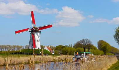 Naklejka premium Damme, West Flanders / Belgium - May 2013: A tourist boat crossing the canal between Brugges and Damme, with a windmill in the background