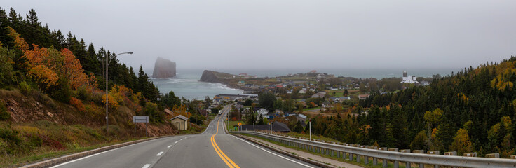 Panoramic view of a road leading to a beautiful modern town on the Atlantic Ocean Coast during a hazy day. Taken in Perce, Quebec, Canada.