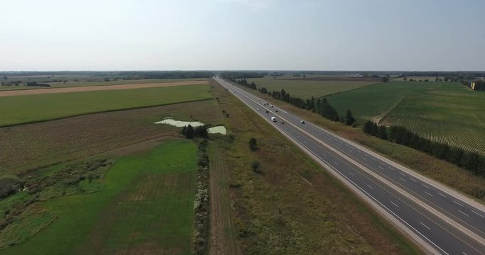 Highway Aerial Traffic Moving Down Highway Over Farmland And Pond Lake In Summertime