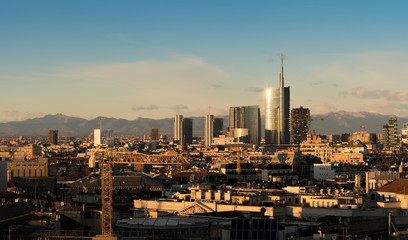 Naklejka na ściany i meble Milan (Italy) skyline at sunset with modern skyscrapers in Porta Nuova business district. Panoramic view of Milano city. The mountain range of the Lombardy Alps in the background.
