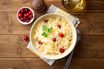 Sauerkraut with cranberries and parsley in bowl on wooden table. Top view.