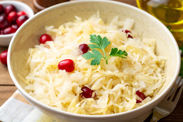 Sauerkraut with cranberries and parsley in bowl on wooden table. Selective focus.