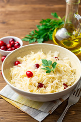Sauerkraut with cranberries and parsley in bowl on wooden table. Selective focus.
