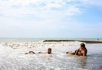 A man and a child are resting on the seashore, sea foam and waves.