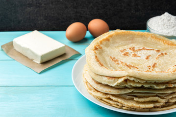 Homemade pancakes blini with flour, eggs and butter on blue wooden background. Russian Maslenitsa,...