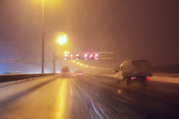 Cars fast drive on the winter speedway or highway with roadway lighting in a snow storm in the twilight when snow with rain is flying. Concept of driving in the dangerous conditions with bad