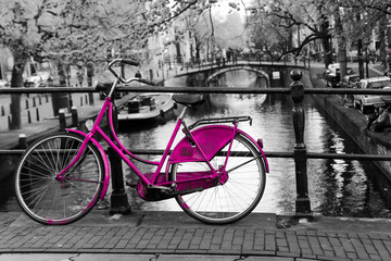 A picture of a lonely pink bike on the bridge over the channel in Amsterdam. The background is black and white. 