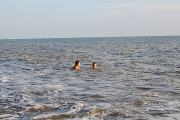 A man and a boy teenager swim in the sea, on big waves