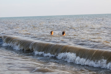 A man and a boy teenager swim in the sea, on big waves