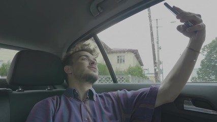 Happy young passenger man taking selfie photos with his smartphone and posting on Facebook while traveling by uber taxi car
