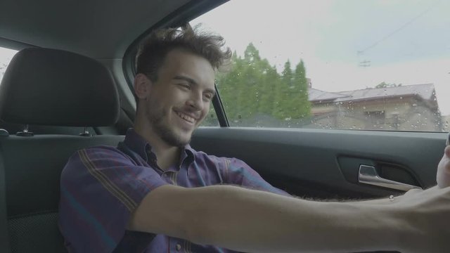 Bored teenager man addicted to smartphone fooling around making grimaces takes selfie pics while he traveling on uber car through city on rainy day