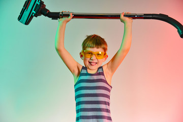 Cute baby raises the hose of the vacuum cleaner, photo in the studio.