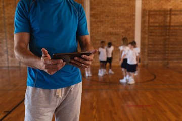Mid section of basketball coach using digital tablet at