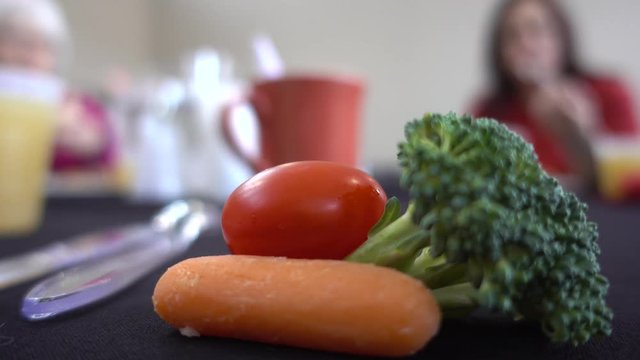 Close Up Of Broccoli And Carrots And Cherry Tomato With People Eating In Background